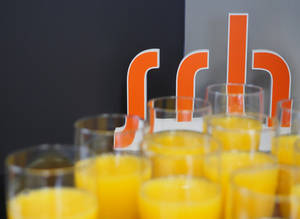 SRH Logo Aufsteller im Hintergrund von Gläsern mit Orangensaft