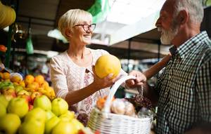 Einkauf auf dem Markt Ein älteres Paar lacht an einem Obststand, während die Frau eine Zitrone hält.